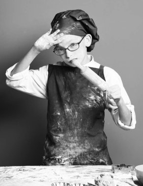 Genç çocuk sevimli aşçı Şef üniforma ve lekeli yüz un tablo kırmızı studio adam üzerinde oklava ile yakın duran gözlüklü şapka