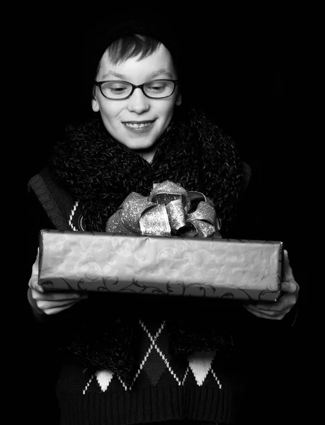 Pequeño niño sonriente o lindo niño nerd en gafas, sombrero y bufanda de punto de moda sobre fondo negro sostiene caja de regalo rojo con oro bo —  Fotos de Stock