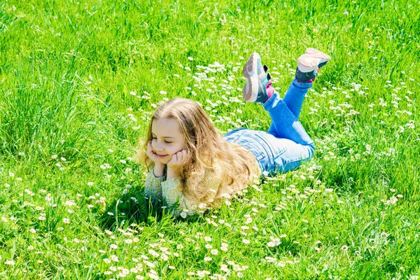Peace and tranquil concept. Girl on calm face spend leisure outdoors. Child enjoy spring sunny weather while lying at meadow. Girl lying on grass at grassplot, green background