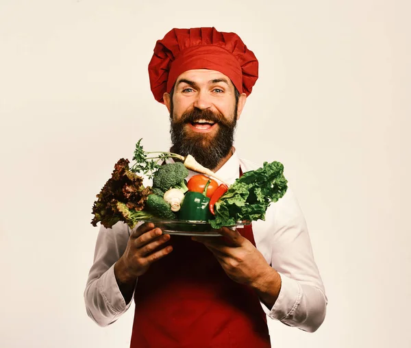 Cook with cheerful face in burgundy uniform holds salad ingredients