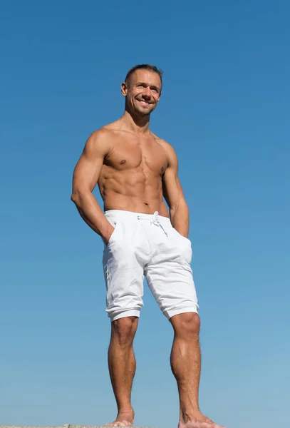 Sportsman muscular belly posing. Man muscular body posing confidently with hands in pockets. Sport and bodycare. Muscular masculine guy look confident. Man sexy muscular bare torso stand outdoor