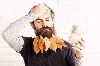 yakışıklı adam şık bıyık ve sonbahar uzun sakal sarı yapraklarda pembe domuz domuz banka ile ciddi yüzünde beyaz tuğla duvar arka plan üzerinde alnına elini sakallı