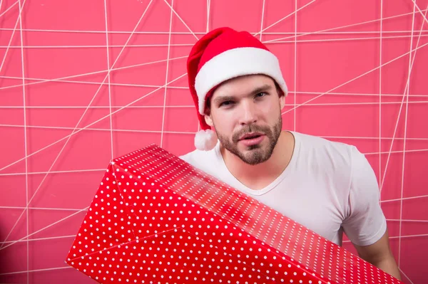 男の魅力的なサンタ クロースは、大きな箱を運ぶ。クリスマス プレゼント交換。クリスマスの休日のお祝い。男ハンサムなひげを剃っていないサンタ帽子は、ギフト ボックスを保持します。クリスマス ギフトの概念。サンタはあなたのための贈り物を持ってください。 — ストック写真