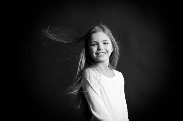 Feliz conceito de infância. Modelo infantil sorrindo com cabelo comprido soprando. Menina com sorriso adorável no fundo escuro. Moda, olha, penteado. Conceito de infância feliz . — Fotografia de Stock