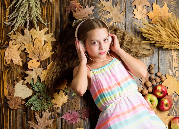 Fall music playlist. Best songs about fall. Enjoy music and relax. Girl lay fallen leaves. Kid listen music headphones wooden background. Child listen music relaxing top view. Fall melody concept