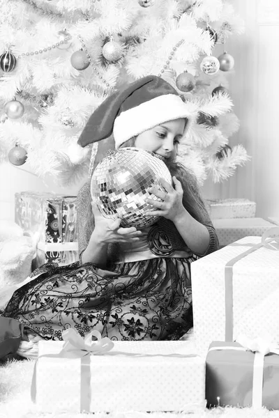 Dziecko w Santa hat w pobliżu prezenty. Dziewczyna z nieśmiałym uśmiechem — Zdjęcie stockowe