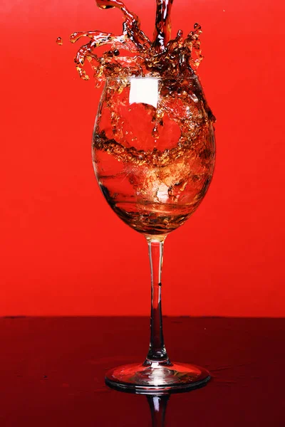 Respingo de bebida em copo de vinho no fundo vermelho, side vie — Fotografia de Stock