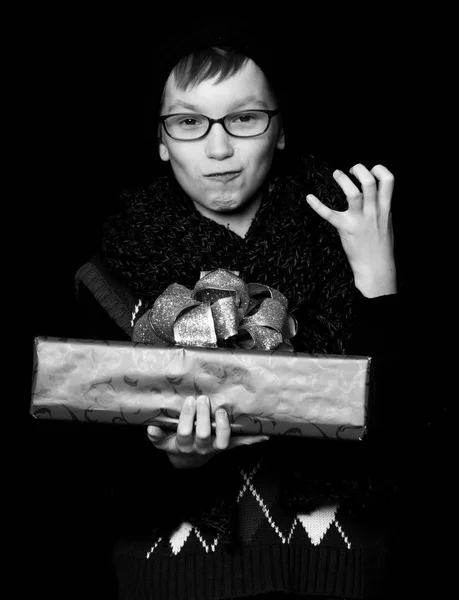 Petit garçon souriant ou mignon nerd kid en lunettes, chapeau et foulard tricoté à la mode sur fond noir tient boîte cadeau rouge avec bo doré — Photo