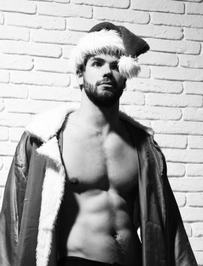 Seksi Noel adam kırmızı santa claus şapka ve kaslı çıplak gövde beyaz tuğla duvar adam üzerinde paltoyla şık sakallı genç yakışıklı sakallı