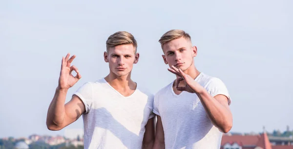 Mannen sterke gespierde atleet bodybuilder poseren met vertrouwen in witte shirts. Mannelijkheid concept. Aantrekkelijke tweeling. Sport levensstijl en gezond lichaam. Mannen tweeling broers gespierde jongens hemel achtergrond — Stockfoto