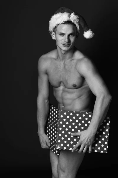 Mladý pohledný macho santa muž se sexy svalnatý sportovní silné tělo má holé torzo a silné břicho v Vánoce nebo Vánoce klobouku pokryt barevné krabičce na zelené studio pozadí — Stock fotografie