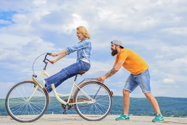 Girl cycling while man support her. Man helps keep balance ride bike. Cycling service. Service and assistance. Mechanic helps maintain bicycle. Supportive service. Woman rides bicycle sky background