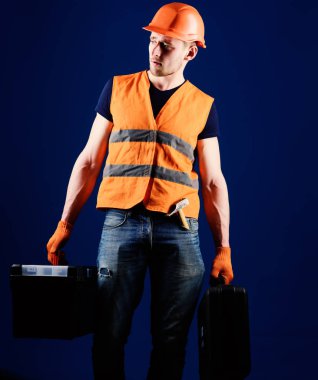 Tamirci, tamirci konsantre yüzündeki profesyonel ekipman ile ağır çanta taşır. Kask, kask içinde adam araç kutusu ve araç, mavi arka plan ile bavul tutar. Profesyonel tamirci kavramı