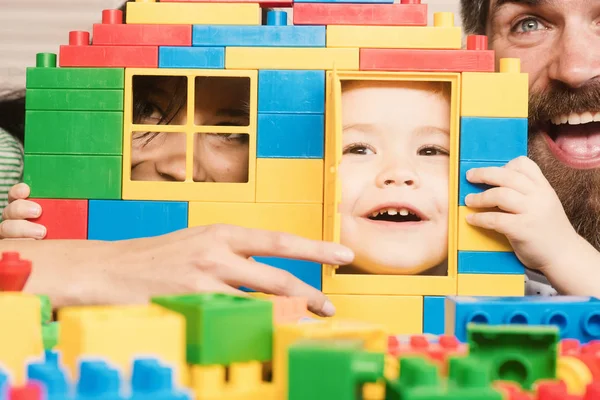 子供と母親は プラスチック製のブロックで作られた家の後ろに隠れます 家族は 一緒に時間を過ごします ひげと口ひげカラフルなレンガで作ったおもちゃの家の近くの父 家族および幼年期の概念 — ストック写真