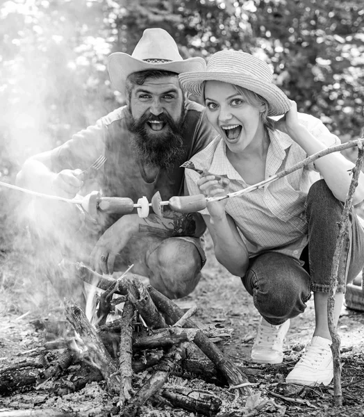 Un paio di turisti affamati arrostire salsicce su bastoni sfondo natura. Coppia innamorata campeggio foresta arrosto salsiccia al falò. Campeggio e pic-nic. Cibo tradizionale arrosto come attributo di picnic — Foto Stock