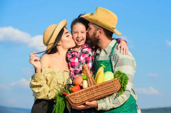 Family gardening. Family farm concept. Parents and daughter farmers celebrate harvest holiday. Family farmers hug kiss kid hold basket fall harvest. Family gardener basket harvest blue sky background