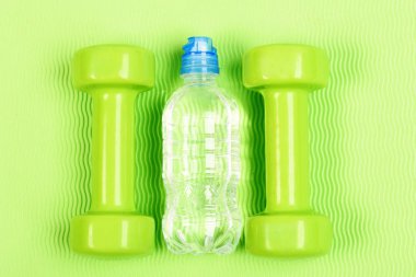 Sağlıklı vücut ve spor eğitim kavramı. İki plastik dambıl ve açık şişe. El ağırlıkları parlak arka plan üzerinde ayarlayın. Yeşil fitness dumbell ve şişe suyu yeşil zemin üzerine çift
