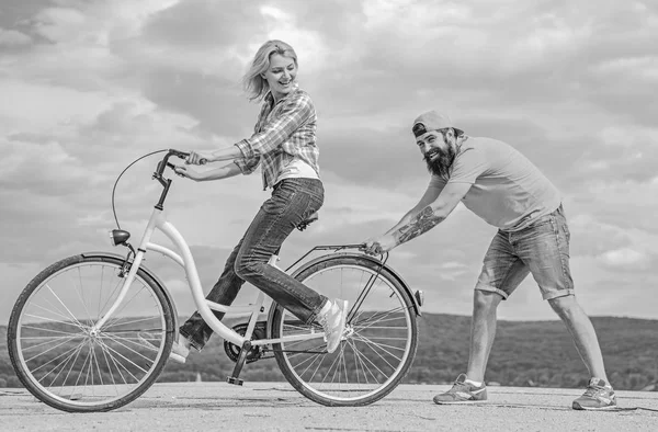 Nauczania dorosłych, jeździć na rowerze. Mężczyzna pomaga zachować równowagę i jeździć na rowerze. Znajdź równowagę. Kobieta jedzie rower na tle nieba. Jak nauczyć się jeździć na rowerze, jako dorosły. Dziewczyna jazda na rowerze, podczas gdy chłopak wspierać ją — Zdjęcie stockowe