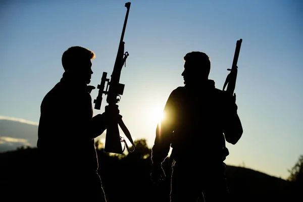 La caza con pareja proporciona una mayor medida de seguridad divertida y gratificante. Hunter amigo disfrutar del ocio. Cazadores amigos guardabosques con armas silueta cielo fondo. Cazadores rifles naturaleza ambiente —  Fotos de Stock