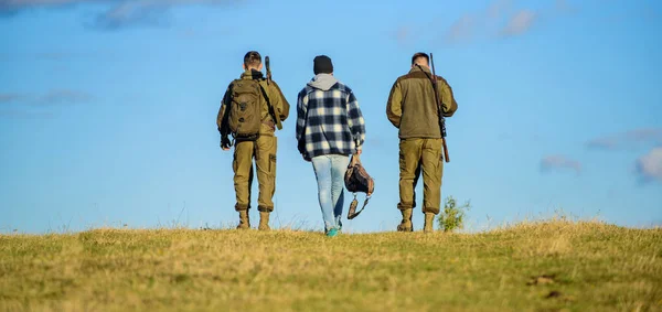 Gli uomini portano fucili da caccia. Caccia come hobby e tempo libero. I cacciatori armati camminano soleggiati giorno d'autunno. Un hobby brutale. I ragazzi si sono riuniti per cacciare. Gruppo uomini cacciatori o guardiacaccia natura sfondo blu cielo — Foto Stock