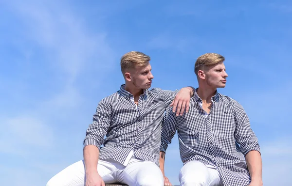 Menswear and fashion concept. Men strong athlete wear same shirts. Brothers twins looks attractive. Fashionable similar outfits. Men twins brothers muscular guys posing in shirts sky background