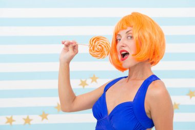 Turuncu saçlı moda kızı eğleniyor. Lolipopu olan havalı bir kız. Seksi bir kadın. Lolipoplu mutlu poster modeli. Oyuncu modunda çılgın bir kız. Şekerci. Hoş görünüş. Oyun zamanının tadını çıkarıyorum. Çok eğlenceli.