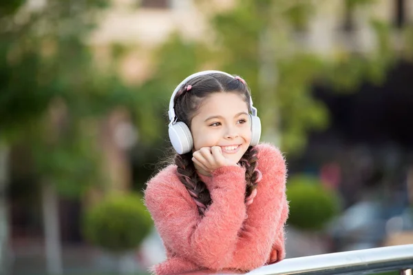 Fajne śmieszne stylowa dziewczyna jest słuchanie muzyki i myśląc o positiveness. Dziewczyna, stojąc na moście z słuchawki. Wpływ spokojnej muzyki. Miła dziewczyna w różowym swetrze ciesząc się piosenki — Zdjęcie stockowe