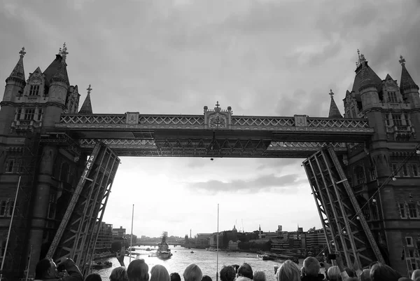 Tower bridge getting opened in London, United Kingdom. People look at bridge over Thames river on grey sky. Architecture and structure concept. Wanderlust and vacation concept — Stock Photo, Image