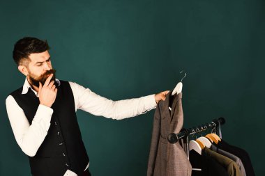 Yeşil arka planda ceketlerin yanında düşünceli yüzlü bir iş adamı.