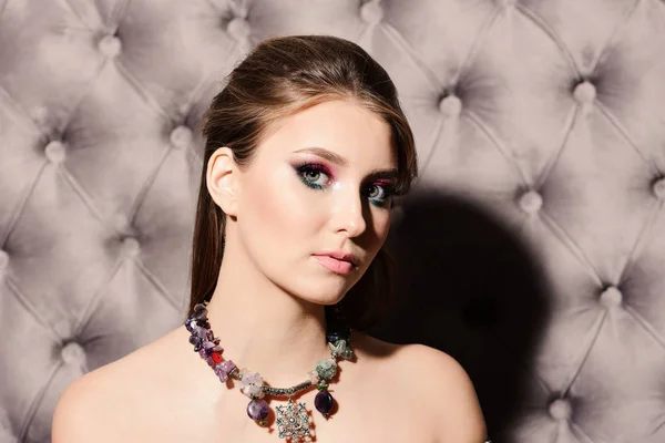 Girl wearing colourful makeup and necklace on grey leather background