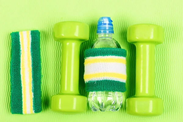 Wristbands, fitness dumbbells and bottle on green background.
