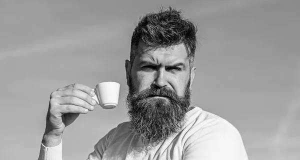 Homem barbudo com caneca de café, bebe café. Conceito de café gourmet. Homem com barba e bigode no rosto rigoroso bebe café, fundo azul do céu, desfocado. Homem com barba longa desfrutar de café — Fotografia de Stock