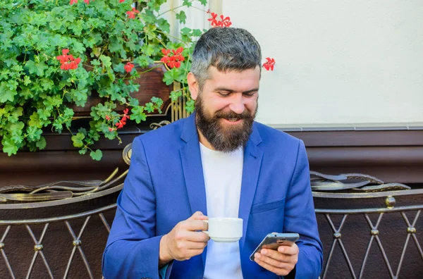 Negocios ventas en línea. Gerente siempre en contacto. Hombre barbudo hombre de negocios sentarse terraza con teléfono inteligente y taza de café. Ocúpate de los negocios incluso mientras disfrutas del café. Hipster trabajo llamada de negocios — Foto de Stock
