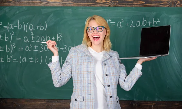 Вчителька в окулярах тримає ноутбук, що серфінгує Інтернет. Освітянка весела дама з сучасним ноутбуком, що серфінгує в Інтернеті крейдяним фоном. Освіта весела. Концепція цифрових технологій — стокове фото