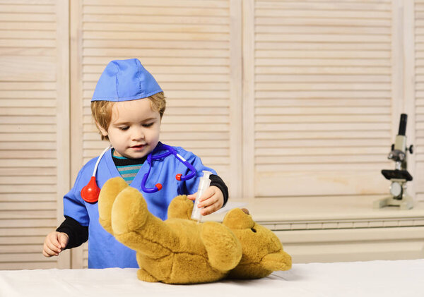 Мальчик в хирургической форме держит шприц на деревянном фоне.