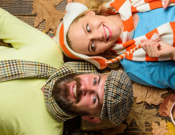 Autumn date concept. Man bearded cheerful face and lady lay on wooden background with leaves top view. Couple in love wear hats scarves enjoy autumn cozy season. Fall date pleasant cozy atmosphere