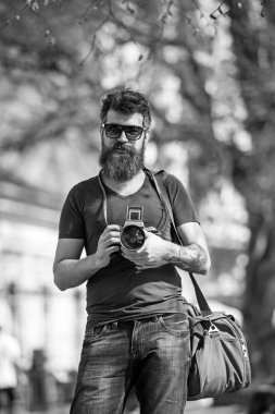 Yüzündeki defocused kendine güvenen, kentsel arka plan, sakallı adam. Sakallı adam omuz çanta taşır ve kamera tutar. Turist kavramı. Yürürken kamera kullanarak uzun şık sakallı