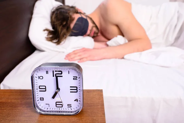 Tippek egészséges alvás. Mielőtt csengő ébresztőóra. Jobban alszik az ember szem maszk. A srác inkább pihenjen a sötétség. Ébresztőóra az éjjeliszekrényen ember álmos borostás szakállas arcát alvás szem maszk háttér — Stock Fotó