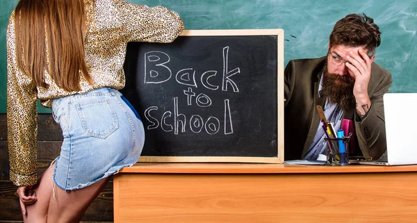 Discipline scolaire et règles de comportement. Professeur indigné assis tableau tableau arrière-plan. Étudiante fille séduit professeur expérimenté. Étudiant en mini jupe avec de belles fesses debout près du tableau noir — Photo