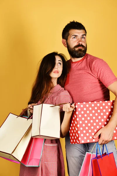 Birbirine aşık çiftler, sarı arka planda alışveriş torbaları bulundururlar.. — Stok fotoğraf