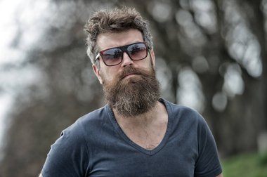 Erkeklik kavramı. Maço bakışla sakal ve bıyık emin acımasız güneş gözlüğü. Sakallı adam katı yüz. Sakal erkeklik özniteliği. Adam sakallı hippi giyim güneş gözlüğü doğa arka plan