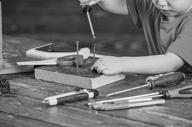 Çocuk meçhul tornavida, ahşap arka plan ile çalışıyor, yakın çekim. Çocuk oyun Oluşturucusu'nu veya Araçlar atölye ile tamirci olarak. Çocuk Çocuk çivi ve vida kullanmayı öğrenir. Eğitim oyun kavramını