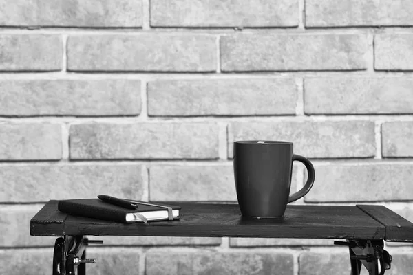 Cup of hot beverage and notebook on small table. — Stock Photo, Image