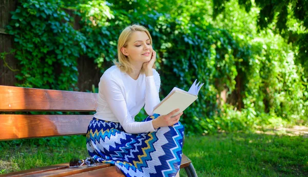 Читання літератури як хобі. Жінка блондинка робить перерву, розслабляючись у книзі читання парку. Найкращий список книг. Дівчина, яка прагне до книги, продовжує читати. Дівчина сидить на лавці, розслабляючись з книгою, зеленим фоном природи — стокове фото