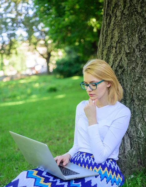 Lady szabadúszóként dolgozik a parkban. Nő laptop működik szabadtéri, park háttérrel. Lány ül fű sovány fa törzse notebook. Wi-fi hálózati kapcsolat ingyenes hozzáférés. Szörfözés internet a természetben — Stock Fotó