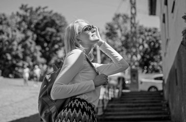 Tüm benimle her zaman gerekir. Trendy kız. Açık havada duran süre sırt çantası taşıyan bir kadın. Şık sırt çantası ile kız yürüyor. Yürüyüş güneşli bir gün, kentsel arka plan kadın güneş gözlükleri tadını çıkarın