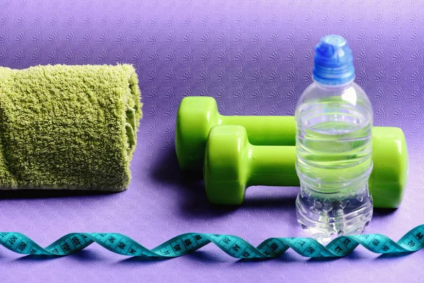 Dumbbells made of green plastic on purple background, close up.