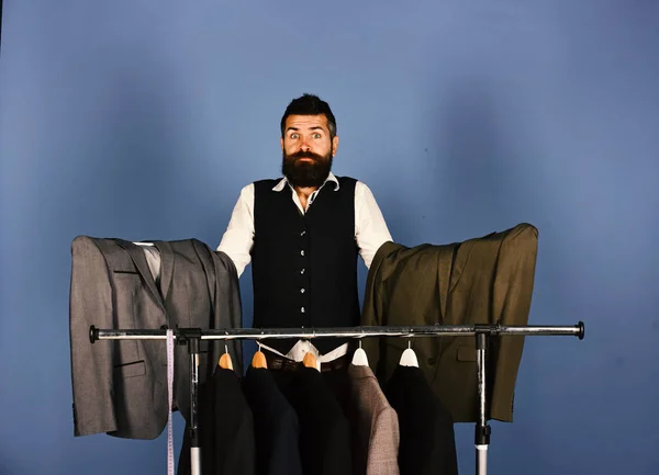 Businessman with confused face holds grey suits near jackets