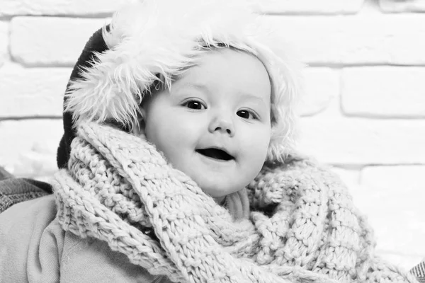 Niño pequeño con adorable cara curiosa en suéter amarillo que pone en la barriga en el sombrero de año nuevo y bufanda de punto en fondo de pared de ladrillo blanco — Foto de Stock