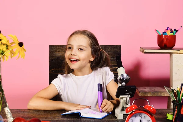 Menina senta-se na mesa com microscópio e despertador vermelho — Fotografia de Stock